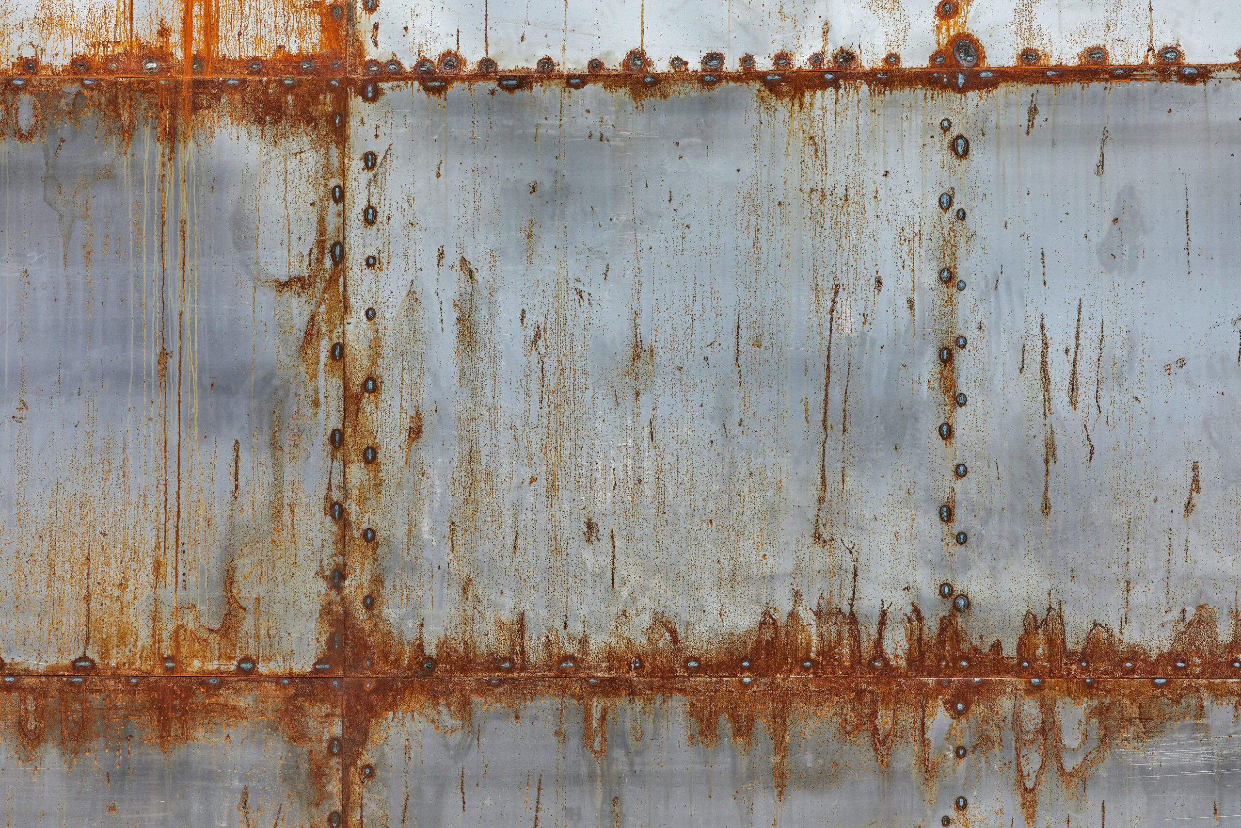 Bare silver steel sheet with orange rust streaks running down from welded seams